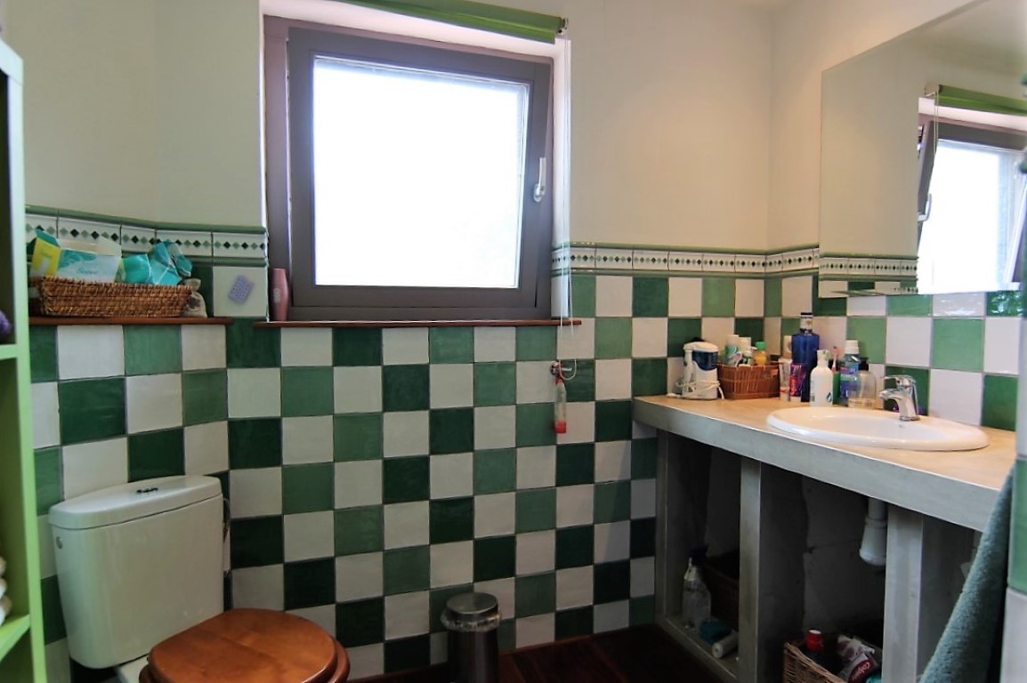 Cuarto de baño con azulejos en damero verde y blanco, lavabo encastrado en encimera de obra y ventana con luz natural.