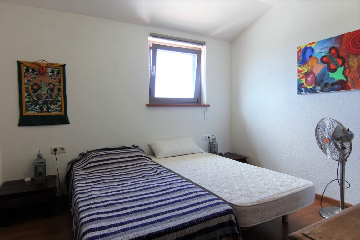 Dormitorio luminoso con dos camas individuales, suelos de madera y paredes blancas decoradas con arte colorido, iluminado por luz natural.