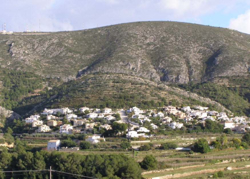Vista panorámica de una ladera aterrazada en Benitachell, con viviendas blancas integradas en el paisaje montañoso y vegetación mediterránea autóctona.