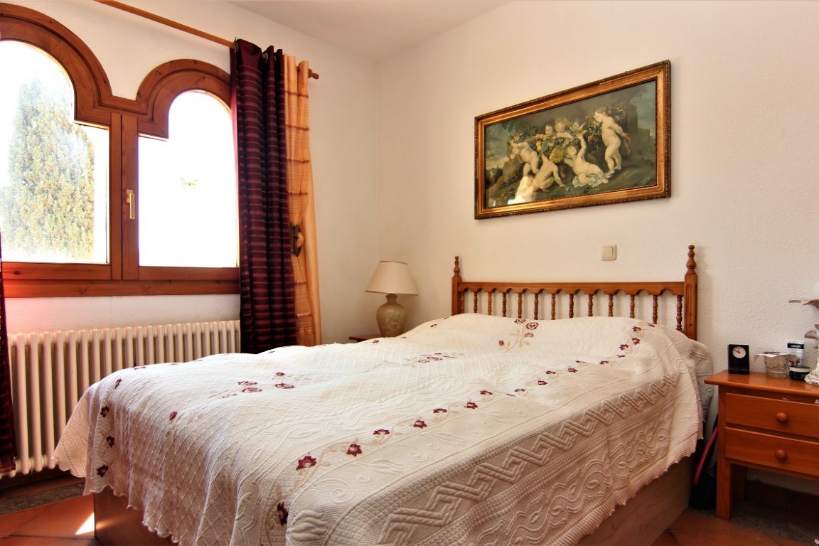 Dormitorio con cama doble, cabecero de madera y ventanas de arco tradicionales. Incluye un radiador clásico, suelos de terracota y abundante luz natural.