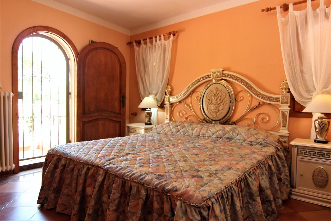 Dormitorio con paredes en tono melocotón, cabecero ornamental de estilo clásico y acceso directo al exterior mediante una puerta de madera en arco.