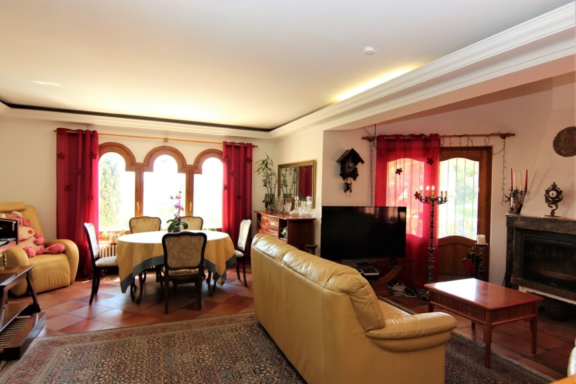 Salón comedor con chimenea de mármol, suelos de terracota y ventanales en arco. El espacio cuenta con iluminación indirecta en el techo y mobiliario clásico.