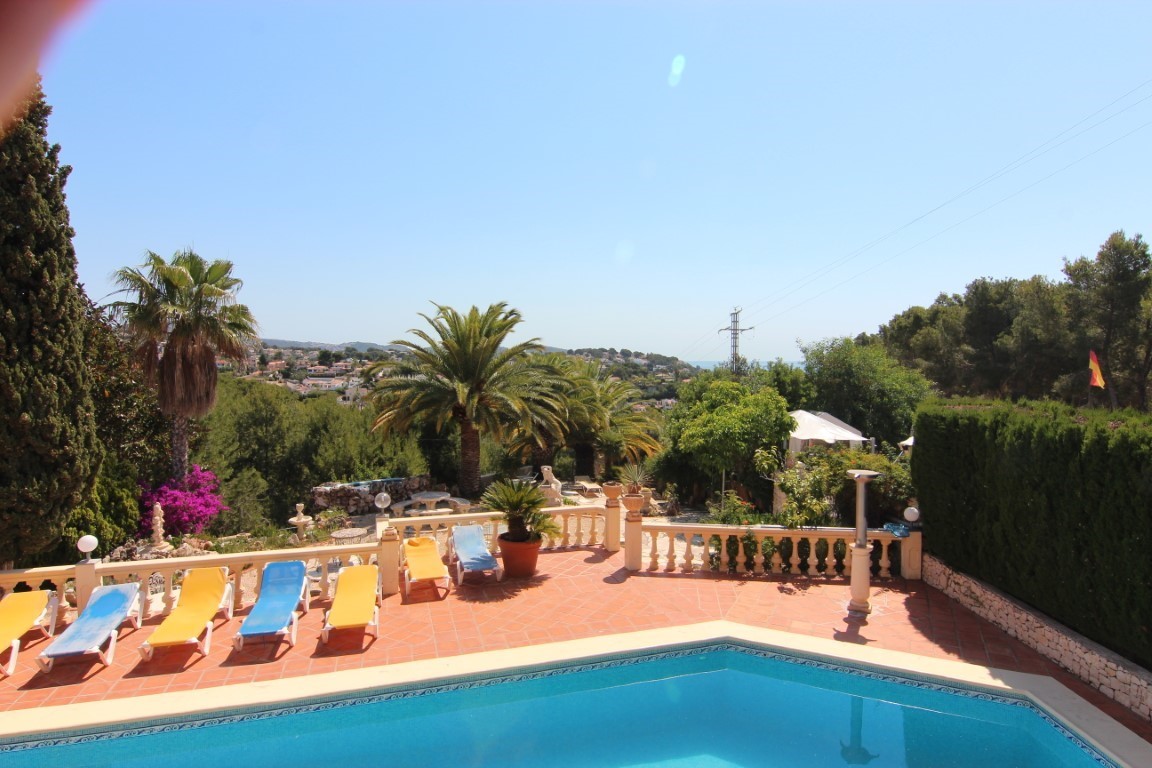 Terraza con piscina rodeada de tumbonas, balaustrada de piedra y vistas despejadas al entorno mediterráneo con palmeras y el mar al fondo.