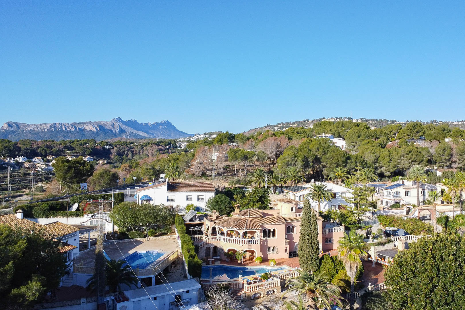 Vista aérea de la villa mediterránea con piscina privada, terrazas arqueadas y una amplia parcela rodeada de vegetación con vistas a las montañas.