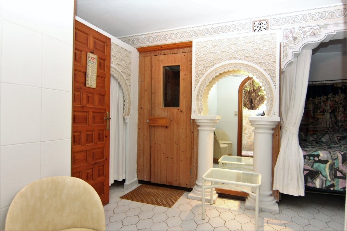 Zona de bienestar con sauna de madera, arcos de estilo morisco con yesería detallada y suelos de baldosas hexagonales.