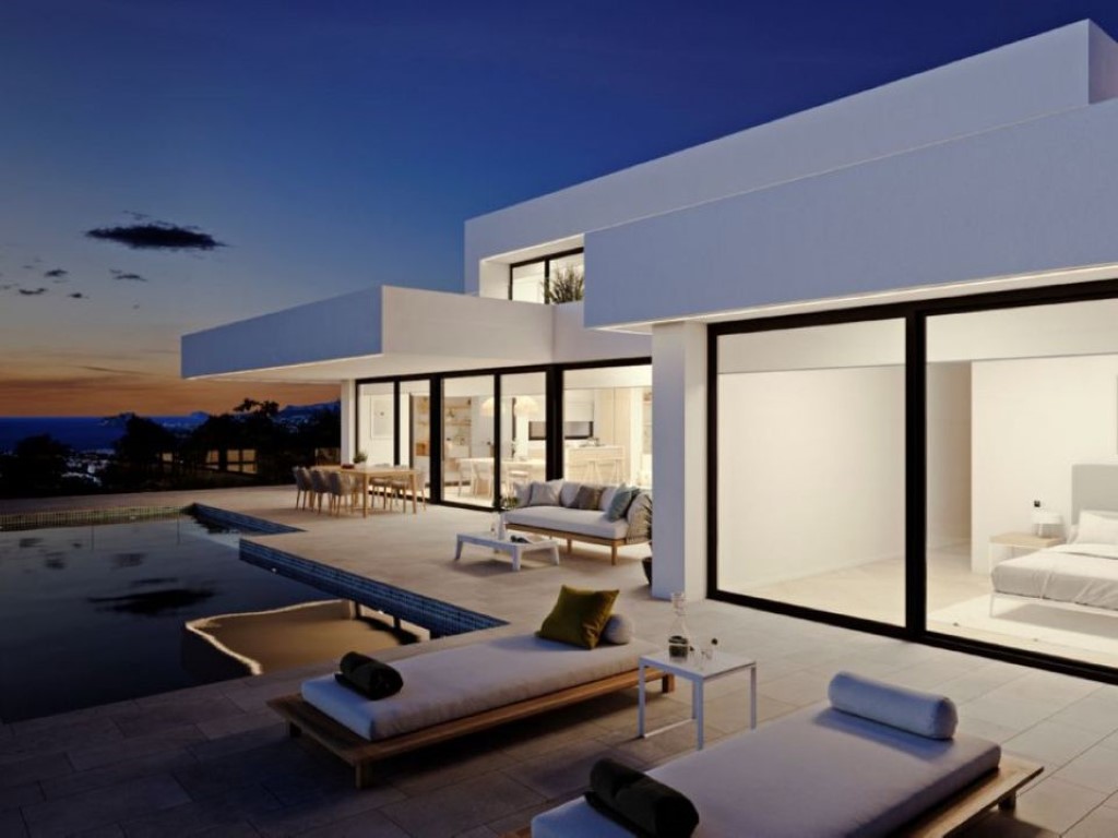 Fachada moderna al atardecer con amplios ventanales, terraza de piedra natural, piscina infinita y vistas panorámicas al mar Mediterráneo.