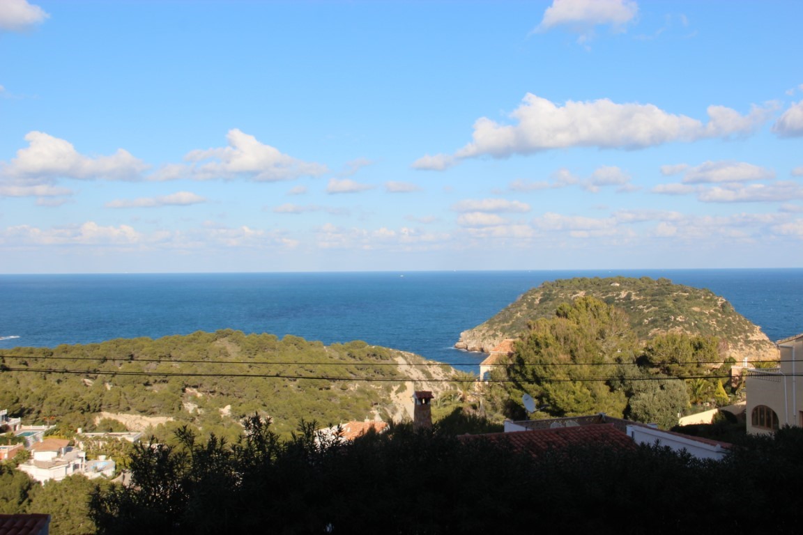 Vista panorámica desde la parcela hacia el mar Mediterráneo y la isla del Portichol, rodeada de vegetación autóctona y tejados tradicionales bajo un cielo despejado.