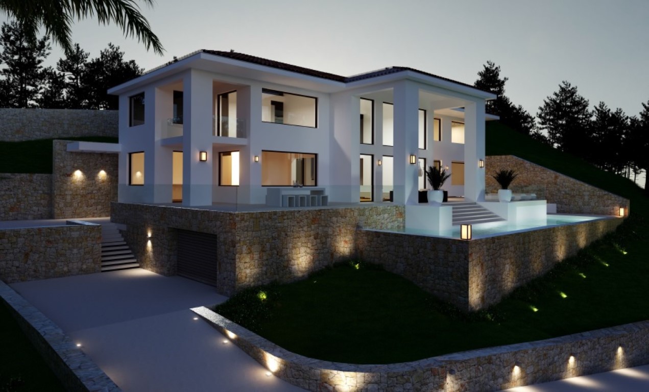 Vista exterior nocturna de la villa con fachada blanca, muros de piedra natural, piscina iluminada y acceso al garaje integrado en el nivel inferior.