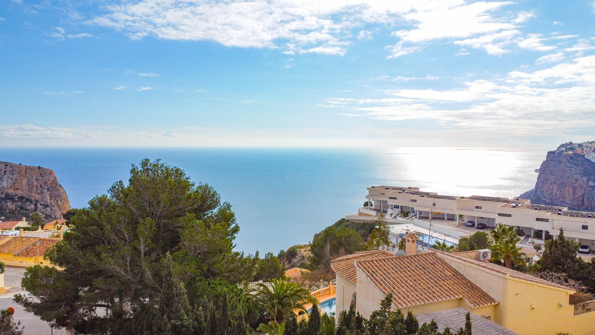Vista panorámica del mar Mediterráneo desde Cumbre del Sol, destacando los acantilados costeros, la arquitectura local y la densa vegetación de pinos bajo un cielo despejado.