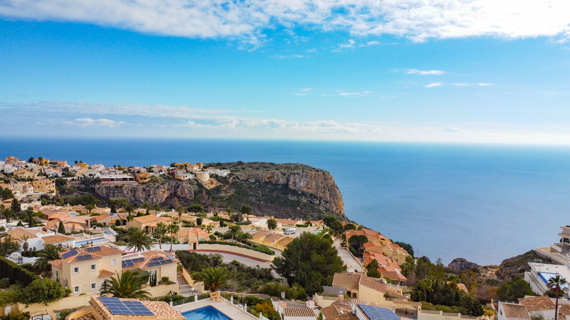 Vista panorámica desde Cumbre del Sol que muestra la arquitectura mediterránea con tejados de terracota y paneles solares frente a los acantilados y el mar.