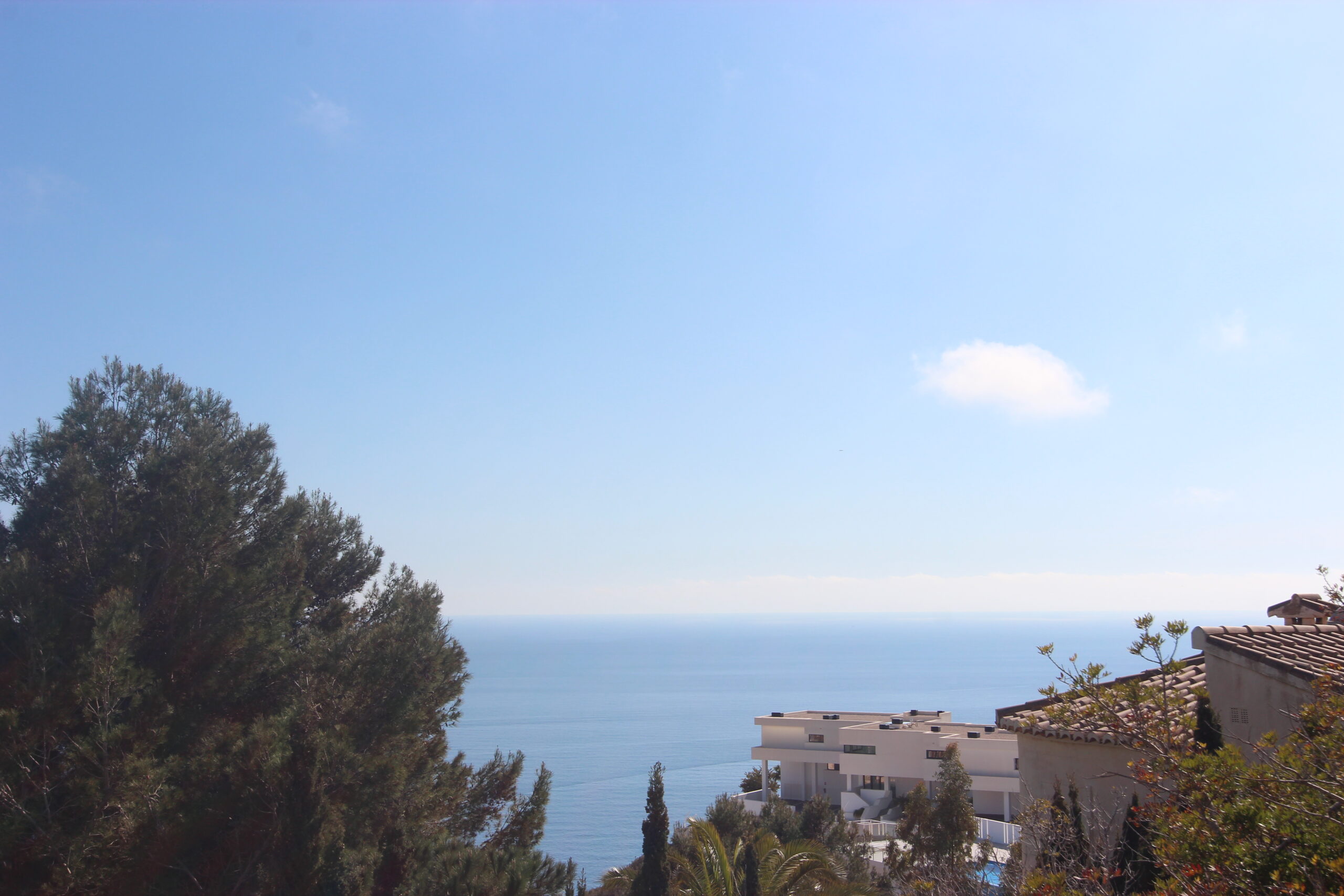 Vistas panorámicas al mar Mediterráneo desde la propiedad, enmarcadas por pinos maduros y arquitectura moderna bajo un cielo despejado.
