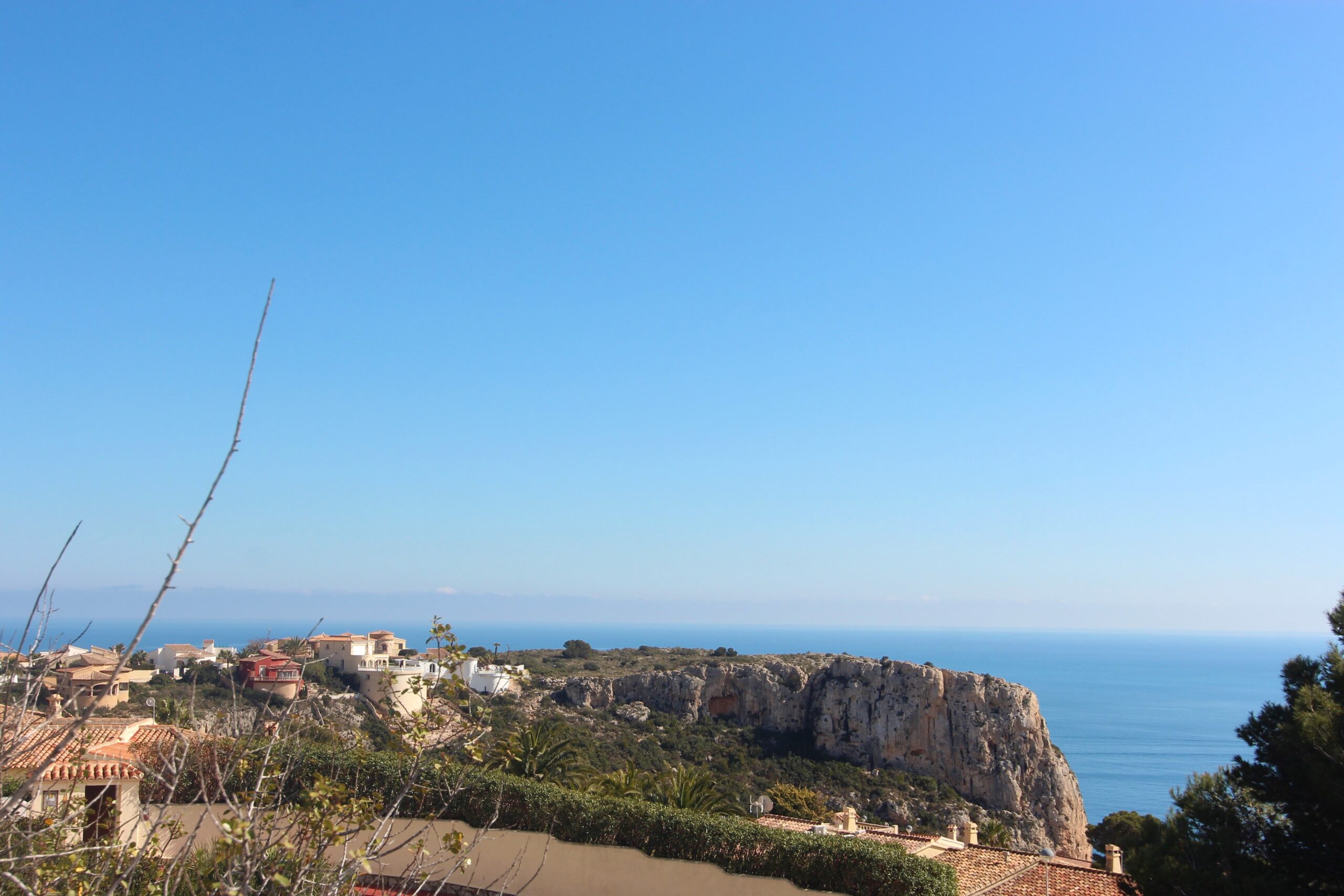 Vistas panorámicas del mar Mediterráneo y los acantilados de Cumbre del Sol desde una posición elevada, rodeada de vegetación autóctona y villas residenciales.