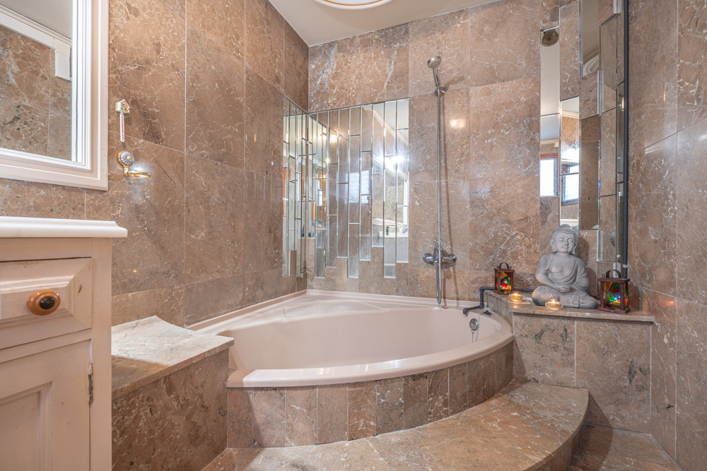 Cuarto de baño de diseño clásico con bañera de rincón, paredes revestidas en mármol veteado y una composición artística de espejos verticales.