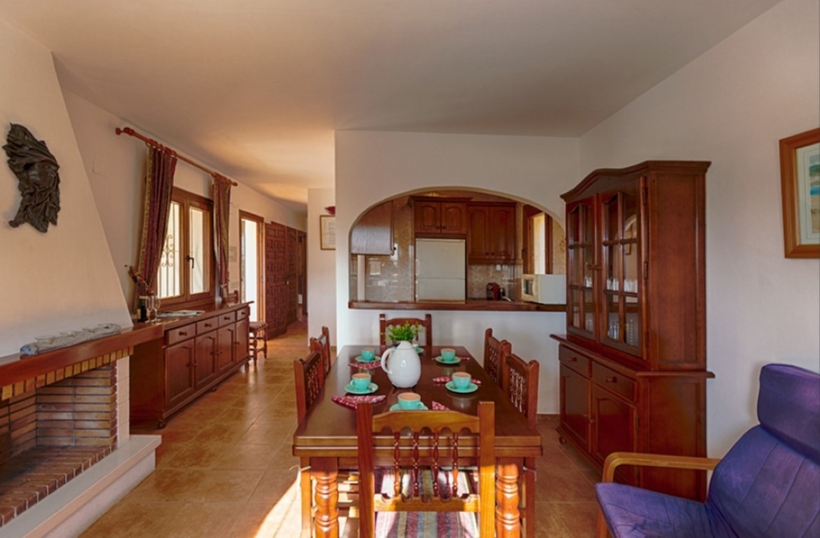 Comedor de estilo tradicional con chimenea de ladrillo, mobiliario de madera maciza y suelos cerámicos. Un arco conecta visualmente el espacio con la cocina.