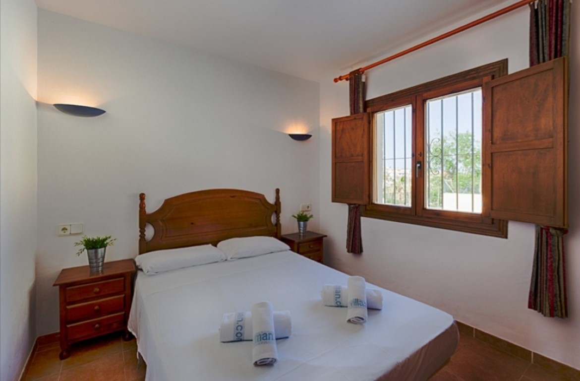 Dormitorio doble de estilo tradicional con mobiliario de madera, apliques de pared y ventana con contraventanas clásicas y rejas de seguridad.
