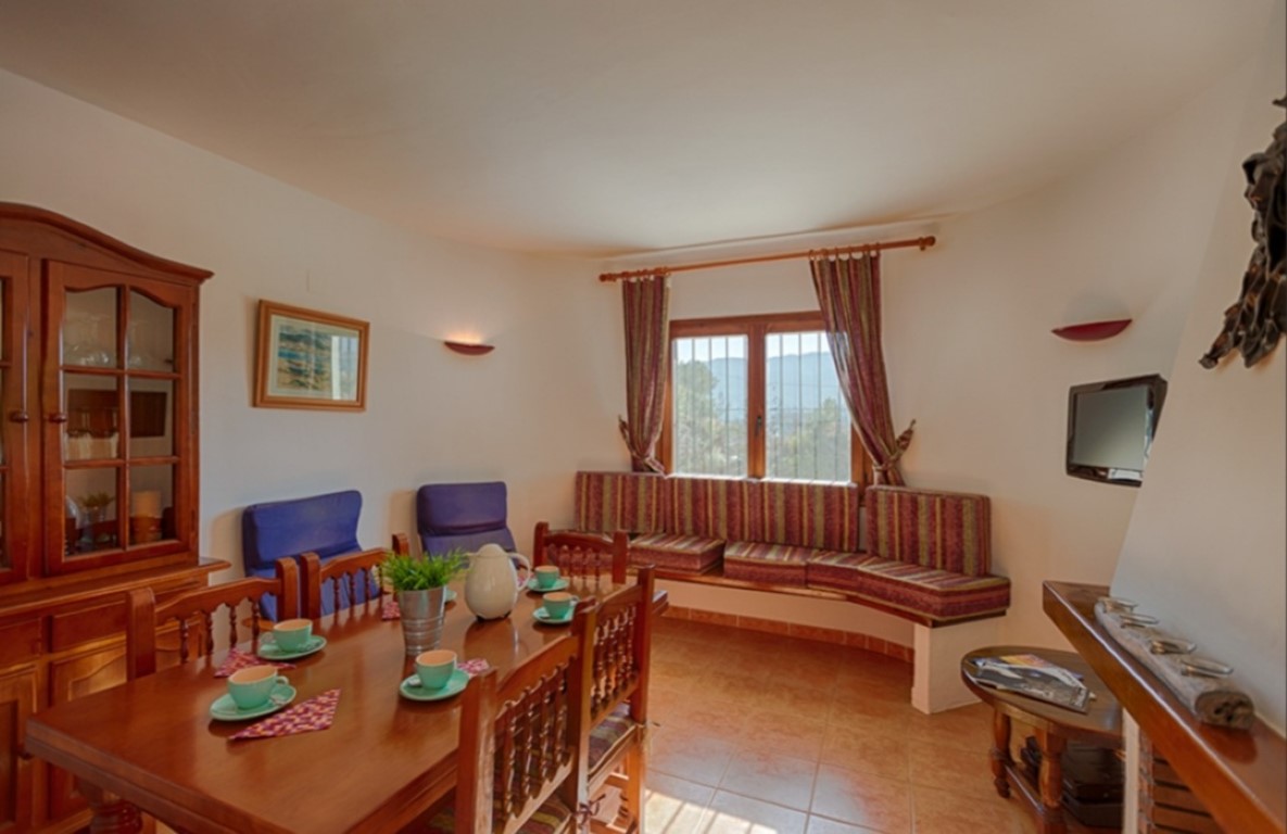 Salón comedor tradicional con mesa de madera, vitrina clásica y un banco de obra tapizado bajo la ventana con vistas al campo.