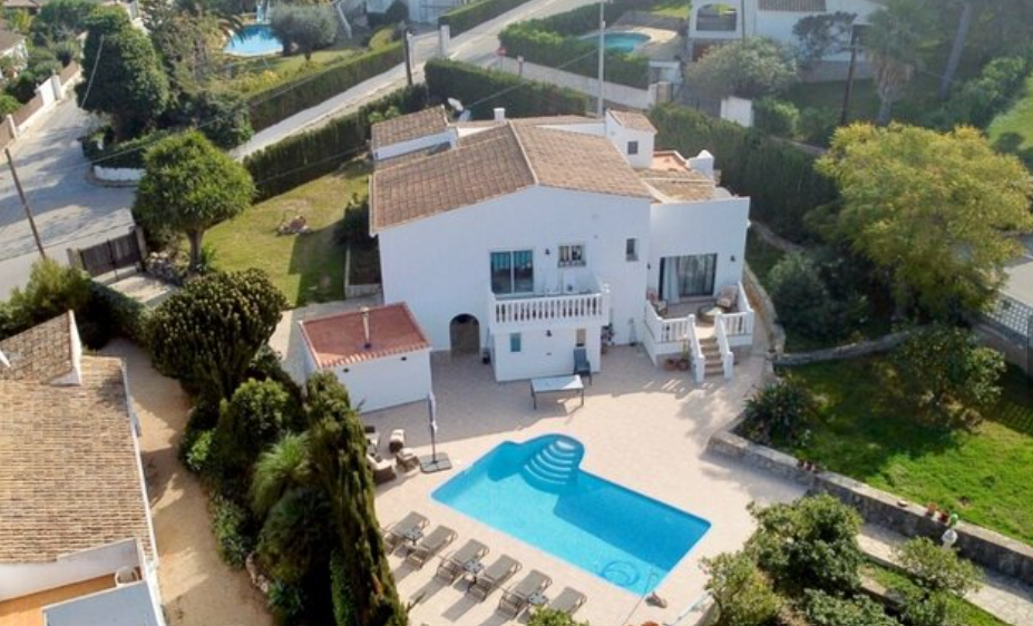 Vista aérea de la villa que muestra la piscina privada, la amplia terraza con tumbonas y el jardín mediterráneo rodeando la fachada blanca tradicional.