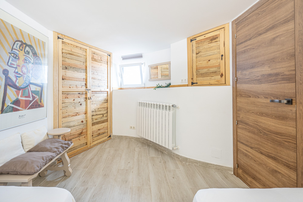 Dormitorio con armarios empotrados de madera rústica, suelos cerámicos de efecto madera, calefacción por radiador y paredes blancas decoradas con arte.