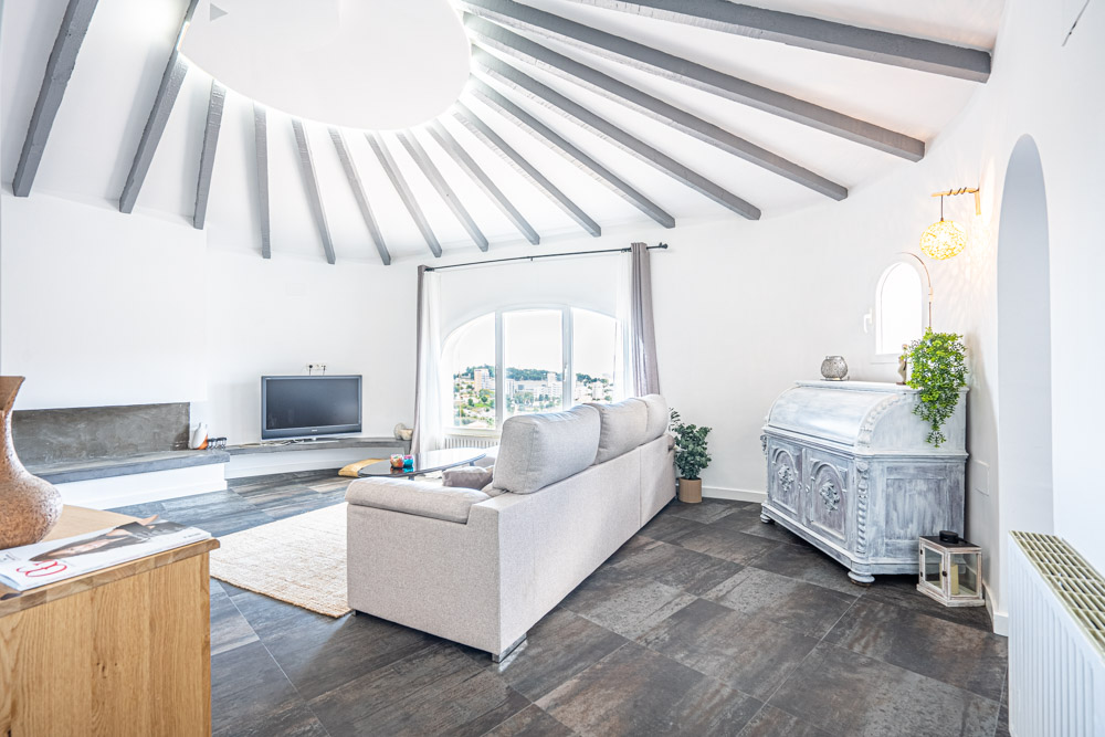 Salón circular con techo de vigas de madera expuestas en abanico, gran ventanal con vistas al entorno urbano y suelos de gres oscuro.