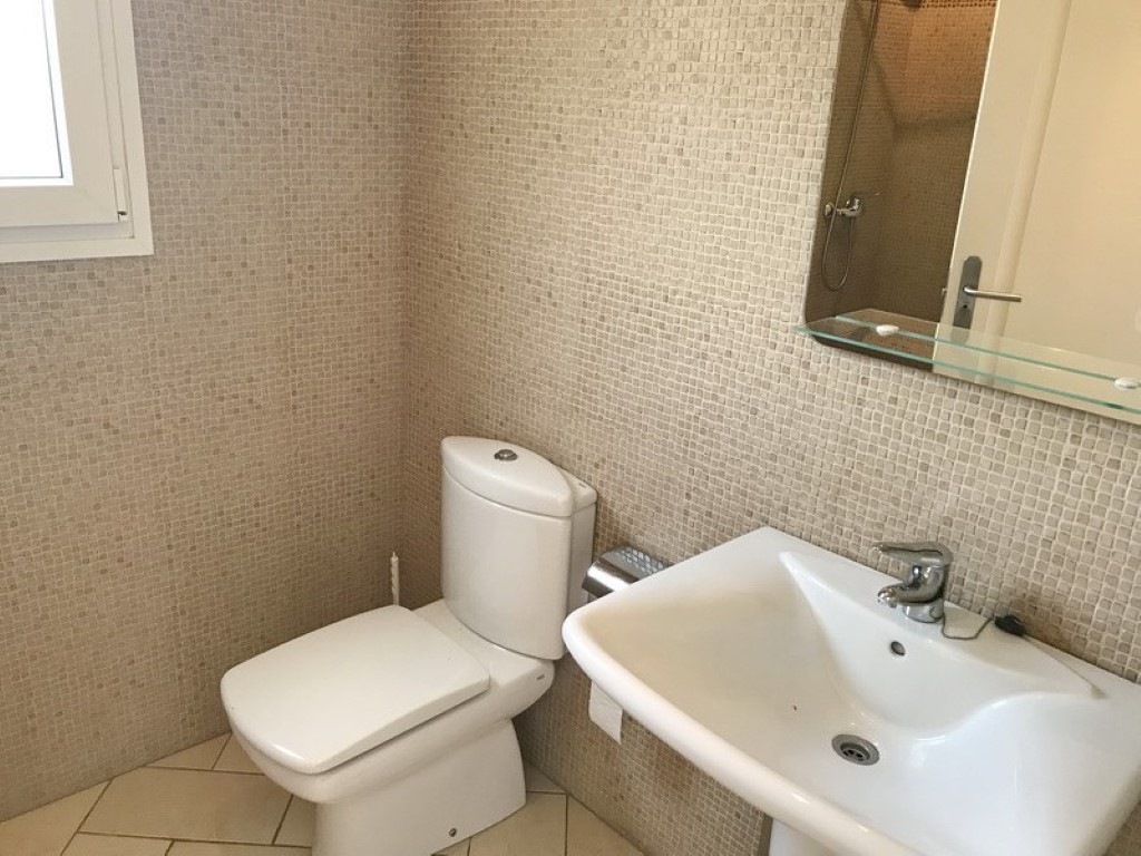 Cuarto de baño con paredes revestidas de mosaico en tonos tierra, lavabo de porcelana blanca y sanitario a juego. Incluye un espejo con estante de cristal y luz natural.