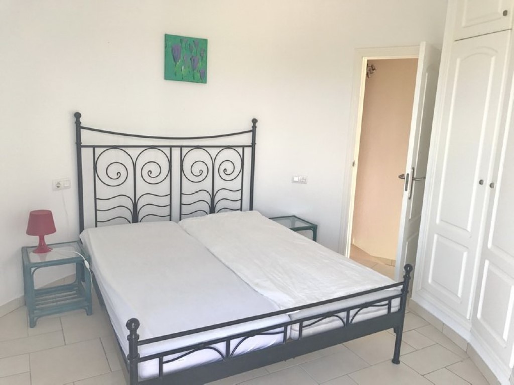 Dormitorio con cama de forja negra, armarios empotrados blancos y suelos cerámicos claros. Incluye mesas de noche con superficie de cristal y una decoración minimalista.