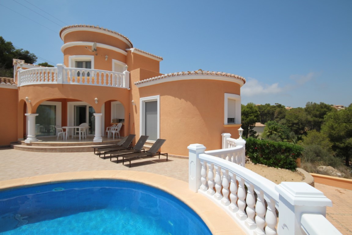 Exterior de la villa con piscina privada, terraza pavimentada y fachada en tonos tierra. Destacan las balaustradas blancas y el porche cubierto con arcos de estilo tradicional.