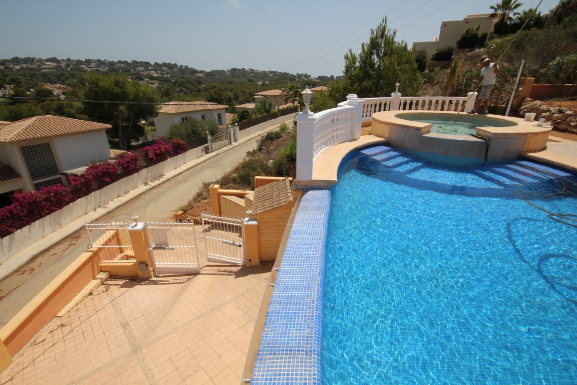 Piscina elevada con gresite azul y jacuzzi circular integrado, delimitada por una balaustrada blanca con vistas panorámicas al valle de Jávea.