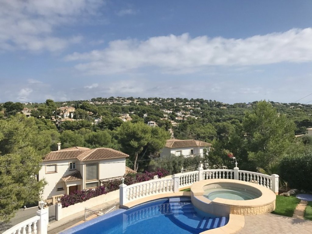 Terraza elevada con piscina de gresite azul y jacuzzi circular integrado, con vistas panorámicas a las colinas de pinos y villas mediterráneas de Jávea.