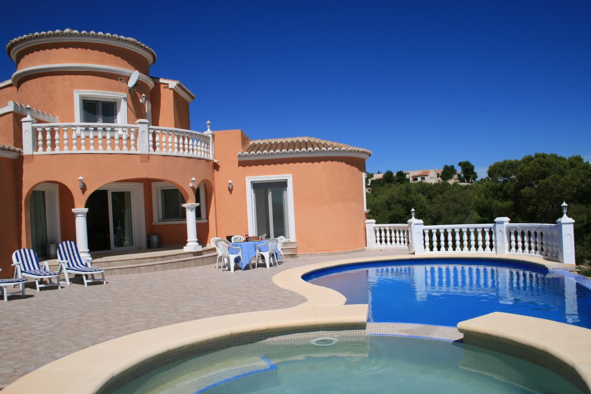 Terraza exterior con piscina de formas curvas, jacuzzi integrado, balaustradas blancas y fachada de tonos terracota con porche arqueado y balcón superior.