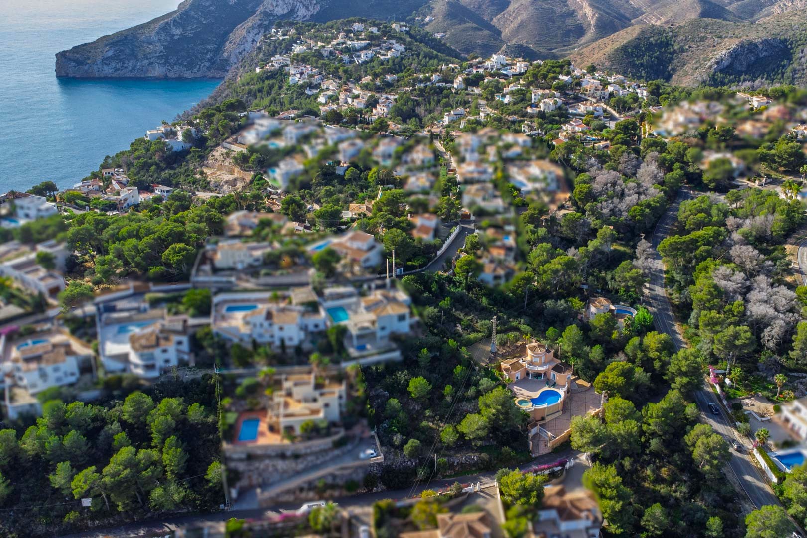 Vista aérea de una zona residencial en Javea, con villas mediterráneas y piscinas privadas rodeadas de densos pinares frente a los acantilados costeros.