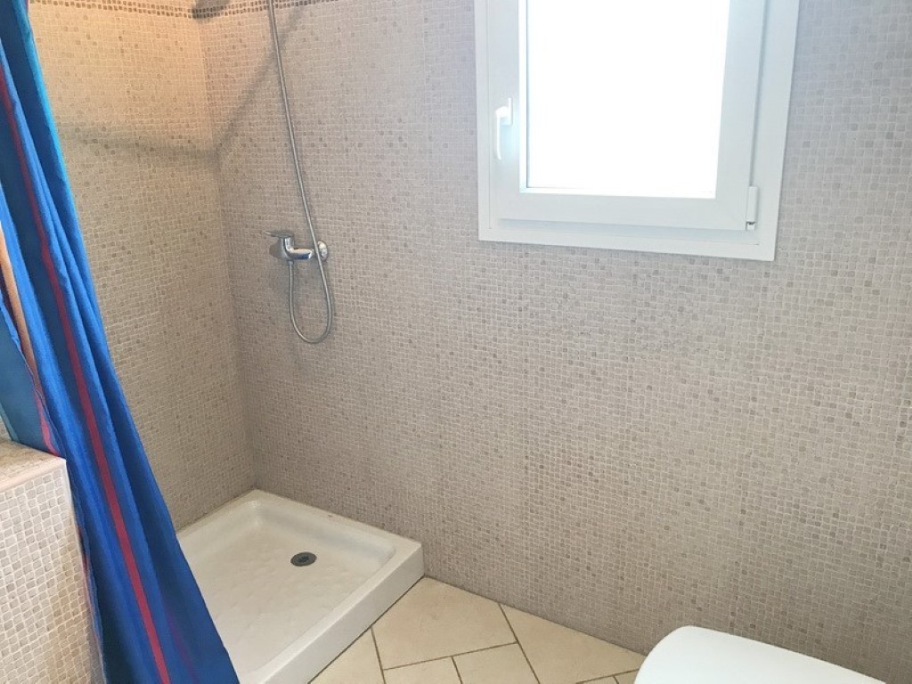 Zona de ducha con paredes revestidas en mosaico beige, plato de ducha blanco y una ventana de cristal translúcido que aporta luz natural.