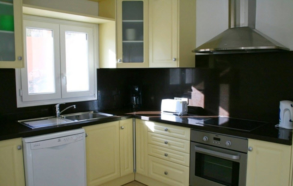 Cocina totalmente equipada con encimera de granito oscuro, armarios en color crema y electrodomésticos integrados de acero inoxidable bajo luz natural.