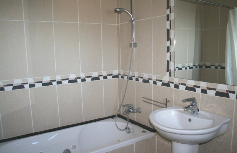 Cuarto de baño equipado con bañera de hidromasaje, lavabo de pedestal y paredes alicatadas en tonos beige con cenefa geométrica decorativa.