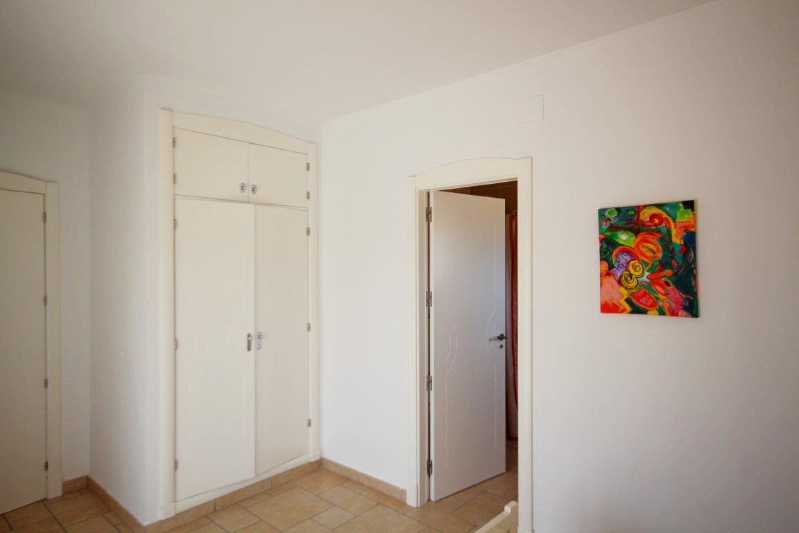 Dormitorio luminoso con armario empotrado blanco, suelos de gres rústico y acceso a una estancia contigua mediante una puerta lacada.