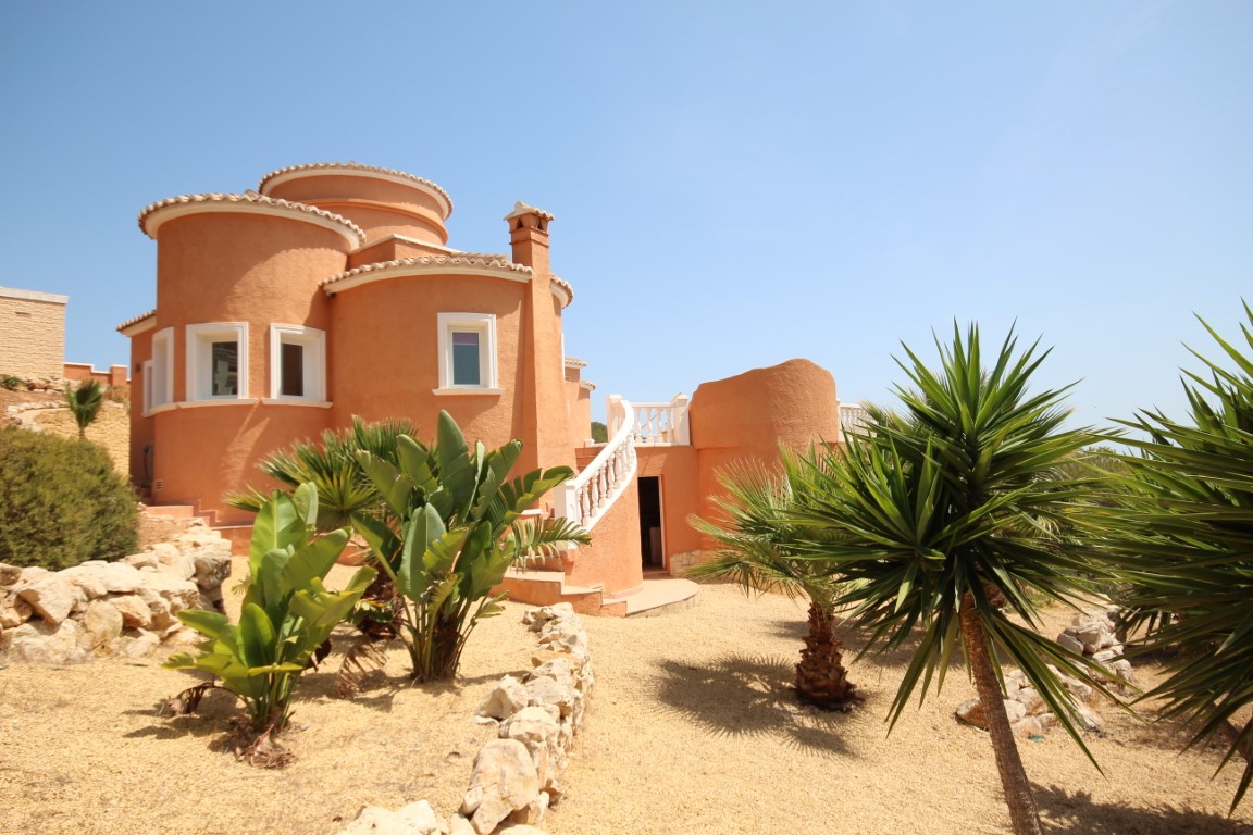 Fachada mediterránea en tonos terracota con formas curvas, escalera exterior de balaustrada blanca y jardín de bajo mantenimiento con palmeras y grava.