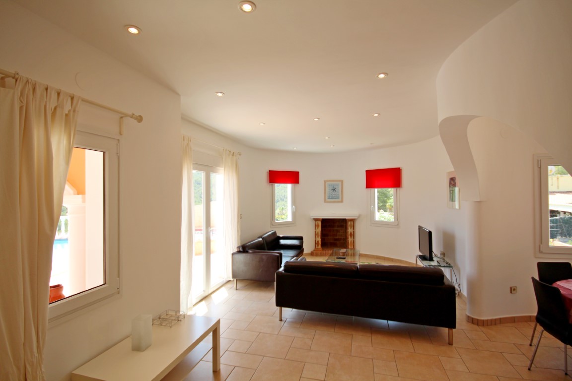 Salón con chimenea de ladrillo, sofás de cuero negro y techo curvo con iluminación empotrada. Grandes ventanales conectan el espacio interior con la terraza exterior.