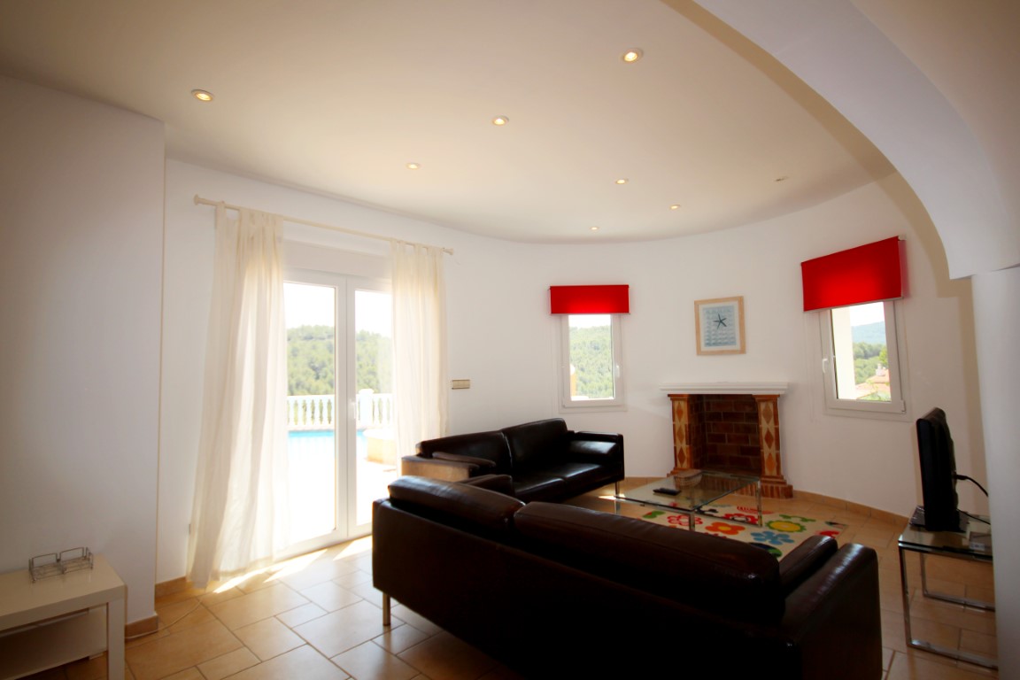 Salón con sofás de cuero oscuro, chimenea de obra y acceso directo a la terraza. Destacan la pared curva, la iluminación empotrada y los suelos cerámicos.
