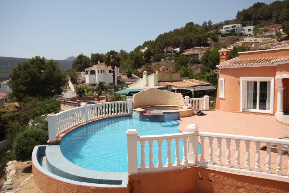 Terraza solárium con piscina infinita de gresite azul, jacuzzi integrado con muro de piedra y balaustrada blanca sobre suelos de terracota.