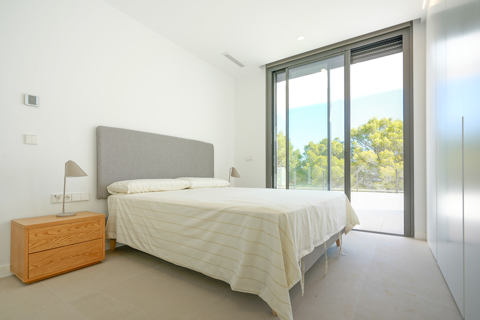 Dormitorio luminoso con armarios empotrados, grandes ventanales correderos y acceso directo a la terraza con vistas al entorno boscoso.