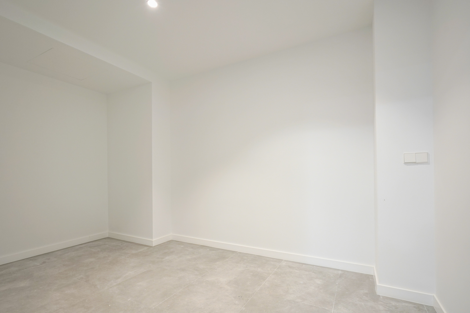 Habitación interior diáfana con paredes blancas, suelos de gres gris y luminaria empotrada, ideal como trastero o sala técnica en la planta baja.