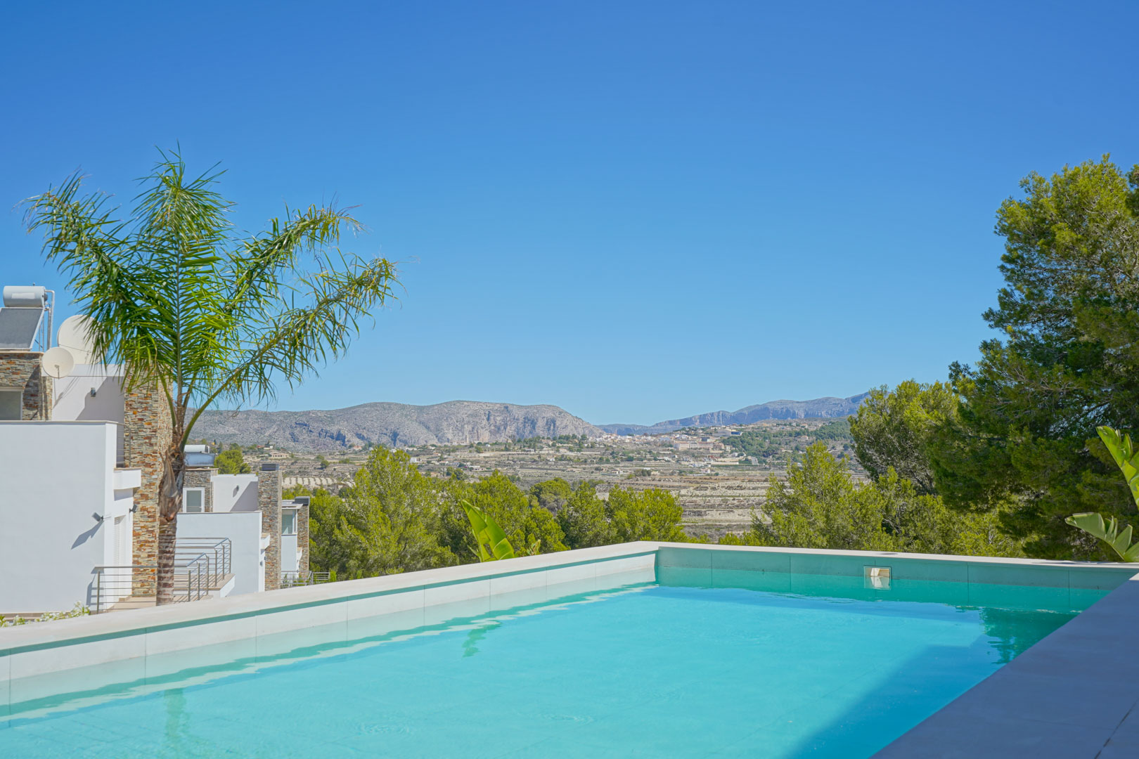 Piscina de borde infinito con coronación de piedra blanca y vistas panorámicas despejadas hacia las montañas y el valle de Moraira.