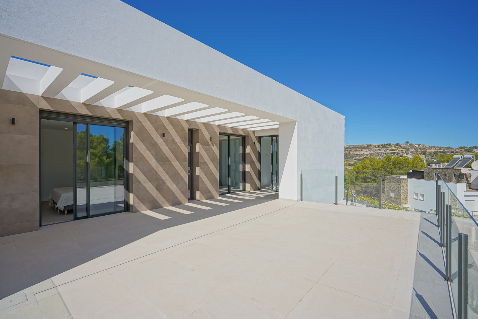 Terraza de la planta superior con pérgola de diseño, barandillas de cristal y acceso directo a los dormitorios a través de amplios ventanales.