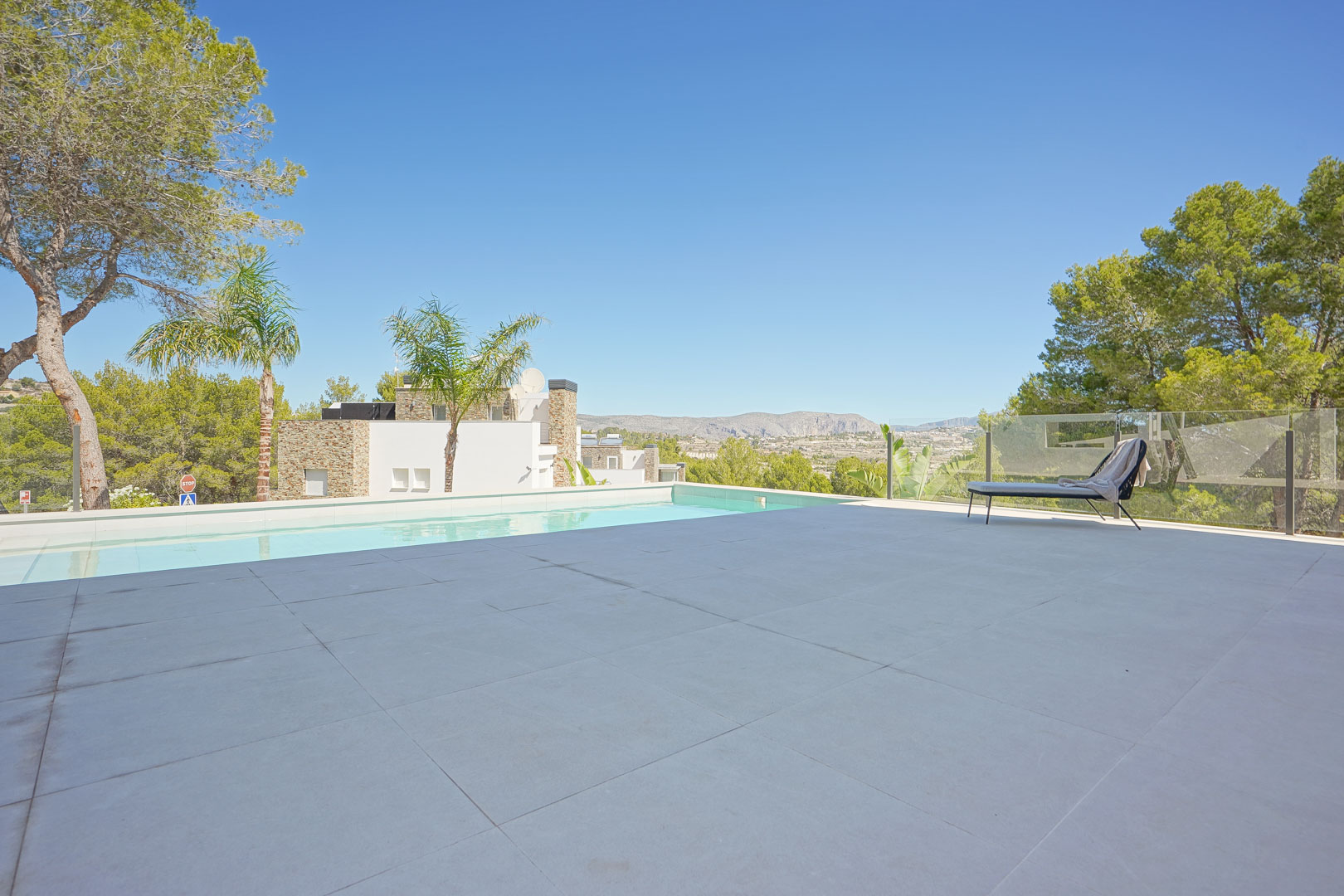 Terraza principal con suelo de gres porcelánico, piscina de borde infinito y vistas despejadas al valle rodeado de pinos mediterráneos.