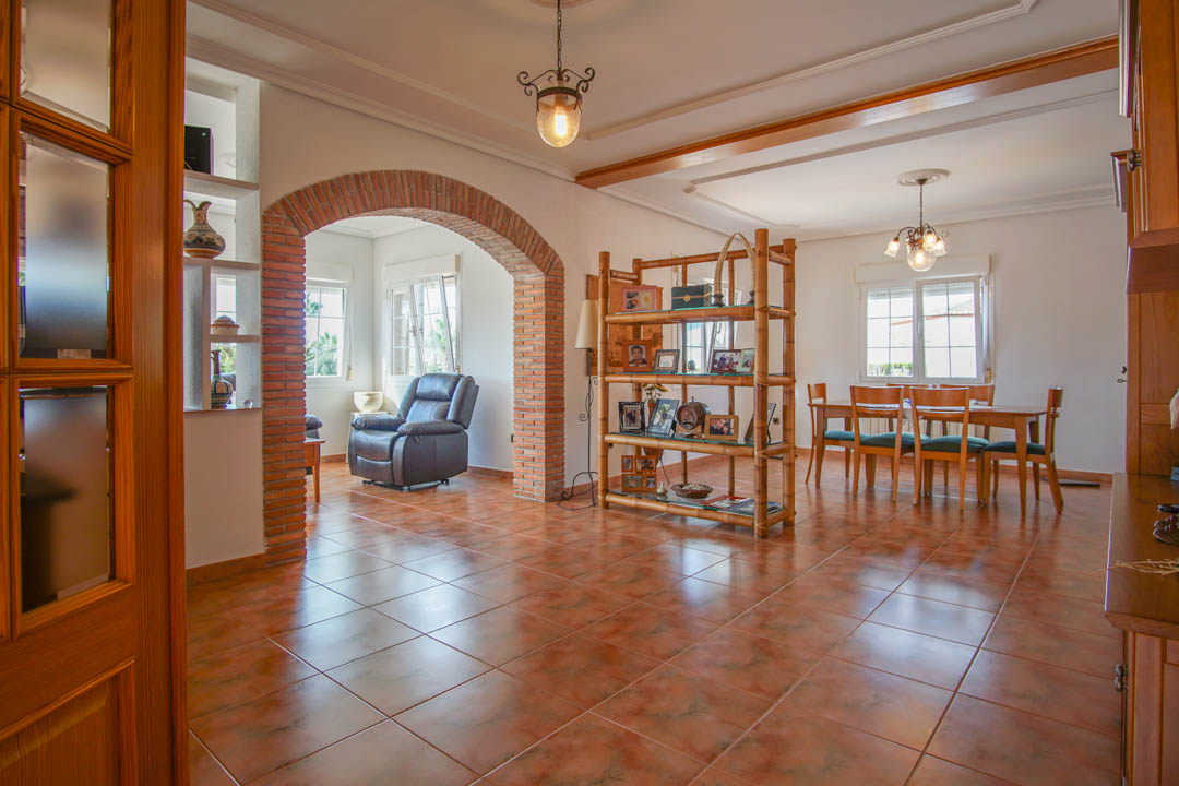 Amplio salón comedor con suelos cerámicos, un arco de ladrillo visto y carpintería de madera maciza. La estancia cuenta con abundante luz natural y techos con molduras decorativas.