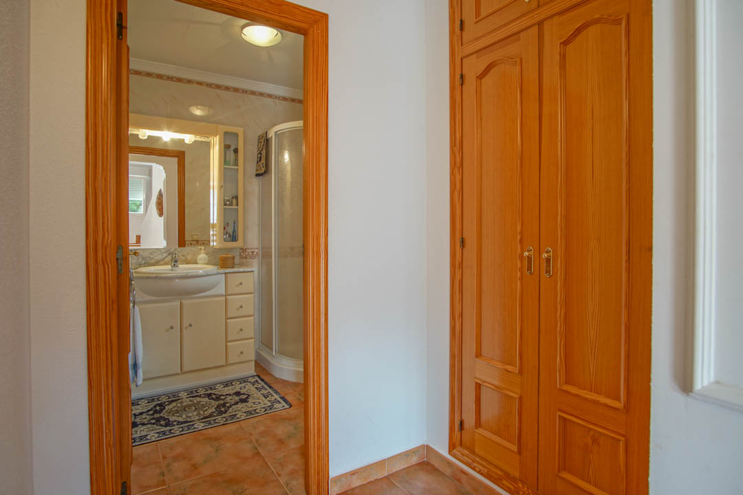 Armario empotrado de madera maciza junto al acceso a un baño completo con encimera de mármol, ducha de rincón y suelos cerámicos.