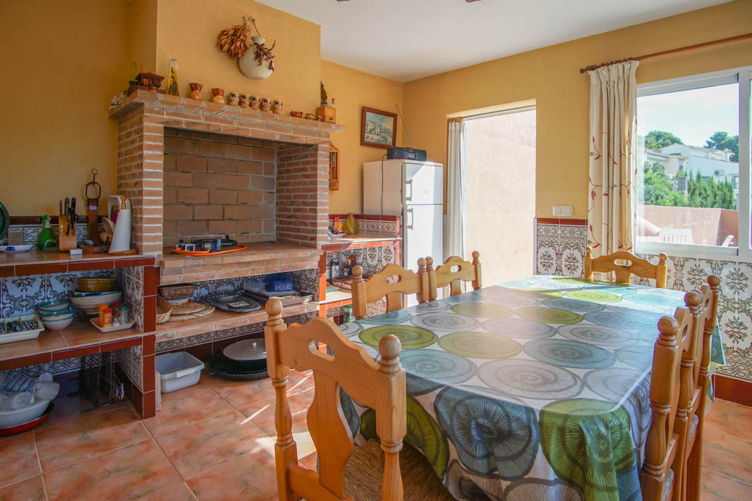 Cocina exterior cerrada con un gran horno de leña de ladrillo, encimeras de azulejos decorativos y zona de comedor con mobiliario de madera maciza sobre suelos de terracota.