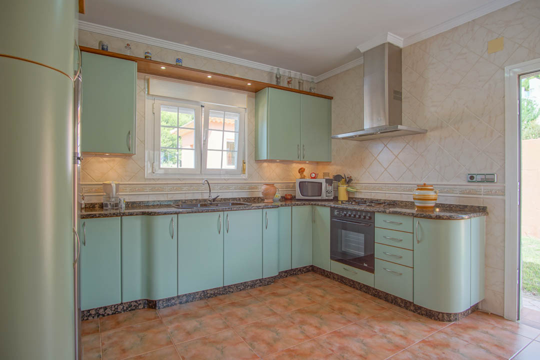 Cocina independiente con armarios en color verde menta, encimeras de granito y acabados curvos. Incluye electrodomésticos integrados y paredes revestidas con azulejos.