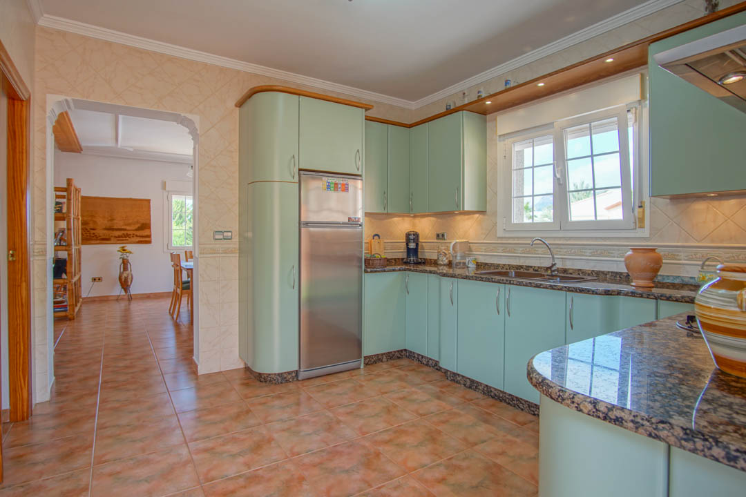 Cocina independiente con armarios en tono verde menta, encimeras de granito y suelos cerámicos. Un arco conecta con el comedor, destacando la luz natural y el diseño funcional.
