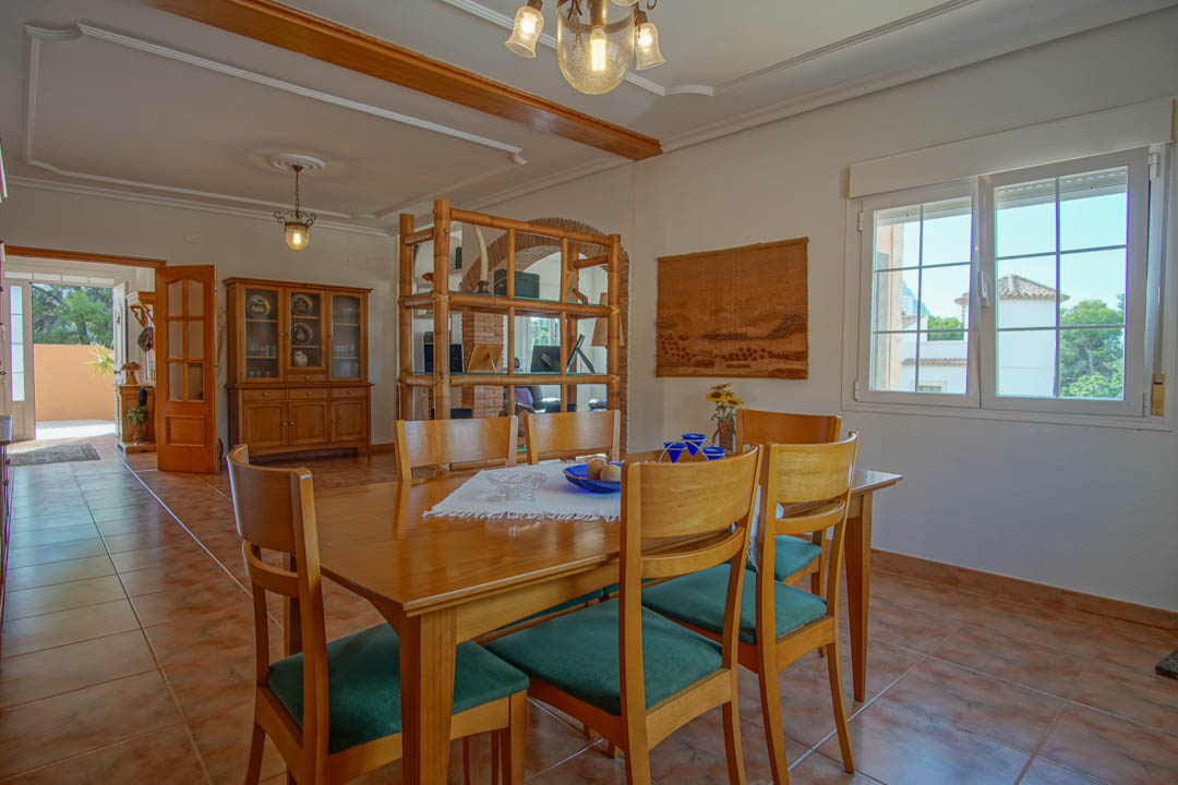 Comedor con mesa de madera maciza, sillas tapizadas y suelos cerámicos. Destacan las molduras del techo, vigas decorativas y un arco de ladrillo visto al fondo.
