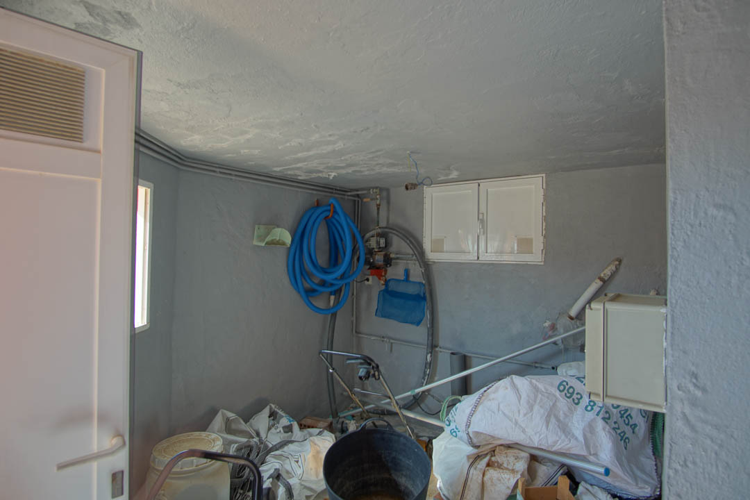 Cuarto técnico y de almacenamiento con paredes grises, equipado con manguera para piscina, conexiones eléctricas y espacio para herramientas de mantenimiento.